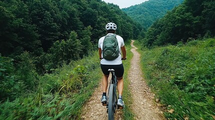 Obraz premium A cyclist rides along a dirt path through a lush green landscape.