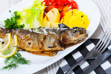 Deliciously baked whole trout with potatoes, tomatoes and greens on white plate