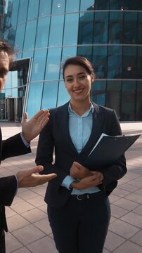4K. UltraHD. POV. Young attractive Businessman in formal suit recommed his partner sexy pretty brownhair lady businesswoman with textpad to You. Modern glass building bg. Teal and orange sunset
