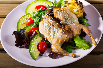 Plate with poultry dish - quail Tabaka with sesame served with salad of avocado and fresh greens