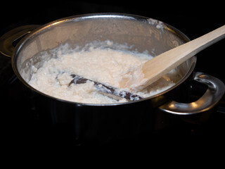 Swedish classic rice pudding with cinnamon stick in a pot with wooden spoon against dark background