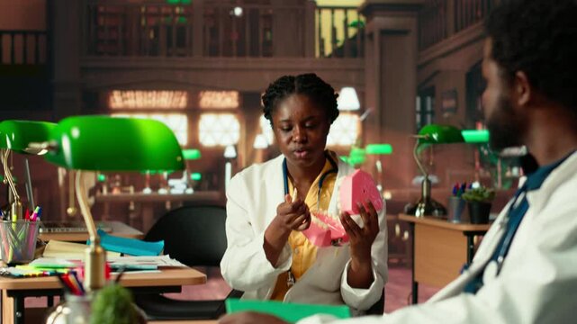 Dentistry students team doing research with plastic human jaw model in a library, preparing for exams on oral hygiene and stomatology. Learning tools for a successful dental career. Camera B.