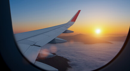 Airplane flying low over foggy mountains, view from plane window of plane wing and sky sunrise