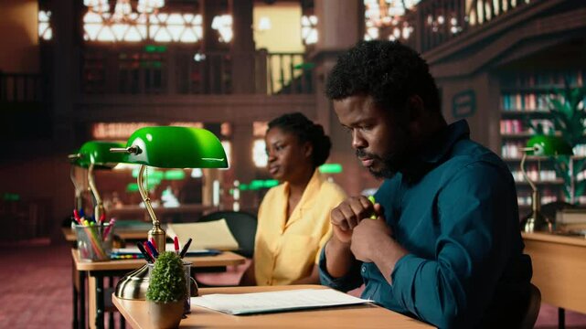Black university student highlighting relevant phrases to learn the summary of the class lesson, memorizing key information by underlining important terms. Academic library. Camera A.