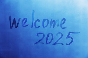 lettering Welcome and numbers 2025 of new year paint with finger on splashed by rain foggy glass on blue window