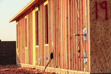 Wood-framed house under construction with exposed studs, plumbing installations, and electrical...