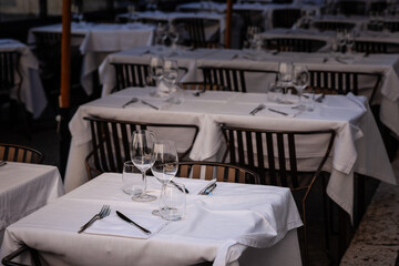 Neatly set tables with white linens stand ready at an open-air Italian restaurant in central Rome. Glassware and cutlery await diners looking to enjoy authentic local cuisine.