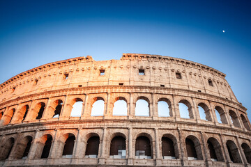 Fototapeta premium Evening sun illuminates the iconic Colosseum in Rome, Italy. The colosseum is a major landmark of rome, an arena and amphitheater from the ancient rome.