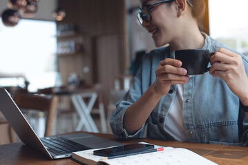 Happy woman drinking coffee during working on laptop computer, remote work at coffee shop. 