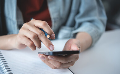 Woman using mobile phone with notebook on office table. Business woman surfing the internet,...