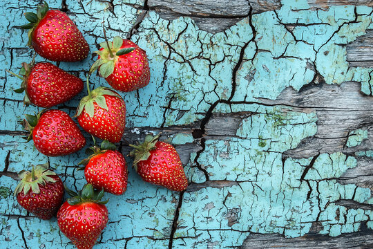 Fresh strawberries scattered on a rustic blue wooden surface with cracks, evoking a vibrant, natural feel