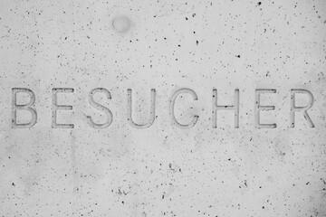 The word Besucher, German for Visitor, engraved in concrete, the letters are a modern sans serif font