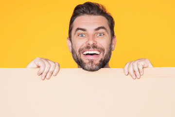 Happy attractive handsome smiling middle aged man showing promo blank board on studio background....