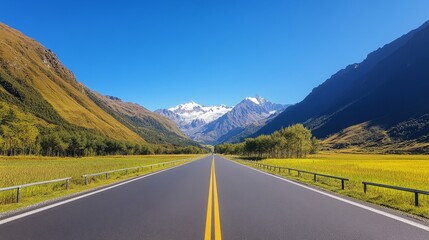 Naklejka premium Expansive Roadway Through Majestic Mountain Landscape Under Clear Blue Sky with Vibrant Green Fields and Golden Rice Paddies Stretching into the Horizon