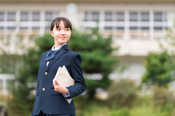 学校の校舎の前に立つ制服姿の中学生・高校生・小学生

