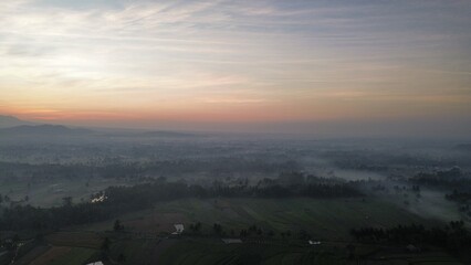 Drone view of rice fields and countryside with mountains background and sunrise and clouds in the morning