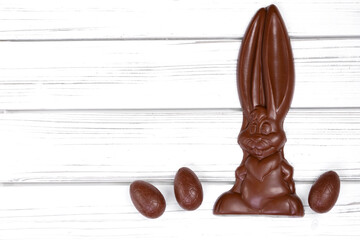 Flat lay of Easter decor on a wooden rustic white table with chocolate big bunny and small eggs around.
