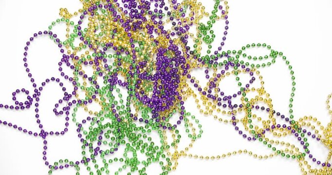 Pile of Mardi Gras beads in yellow or gold green and purple. Throw Mardi Gra bead necklaces covering white background. Celebrating Mardi Gras, aka Fat Tuesday, with the tradition of throwing beads.