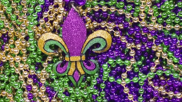 Pile of Mardi Gras beads in yellow or gold green and purple with a large fleur de lis. Throw Mardi Gra bead necklaces covering white background. Celebrating Mardi Gras, aka Fat Tuesday.