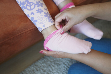 Mother helps child put on pink socks while sitting on a cozy couch at home