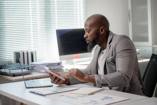 African american professional calculating expenses, reviewing financial paperwork while working at modern office desk