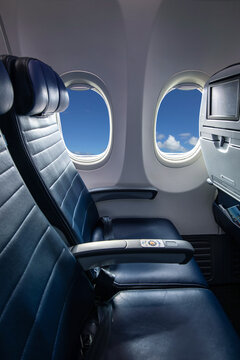 Two interior airplane seats and two windows with clear blue sky
