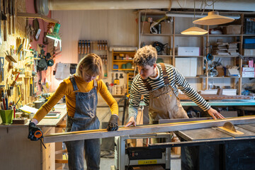 Carpentry colleagues handle circular saw station, measuring wooden beam with precision....