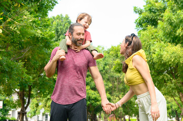 Fototapeta premium Happy Family. father, mother with little child in the park on a sunny summer day together. Son sitting on his father shoulders happy in vacation time.