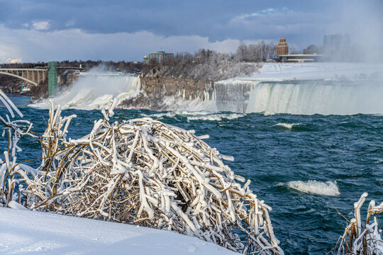 A breathtaking winter scene of Niagara Falls, Ontario, Canada, frozen in time. The cascading waters, partially covered in ice, create a mesmerizing contrast between the deep  river and the white, fros