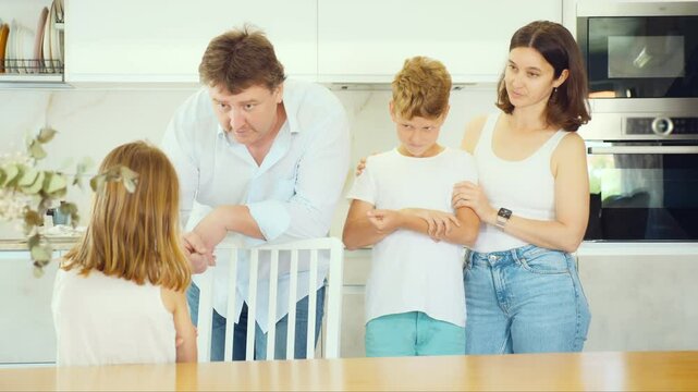 Little girl being scolded by angry parents and preteen brother standing by them in the kitchen. High quality 4k footage