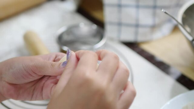 Close-up of hands carefully folding gyoza dough with precision, showcasing the delicate art of making Japanese dumplings, set in a cozy kitchen with tools like a rolling pin and bowl in the background