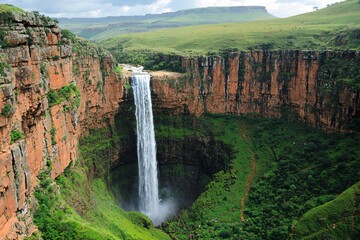 Majestic waterfall cascading down a rocky cliff surrounded by lush greenery and distant hills