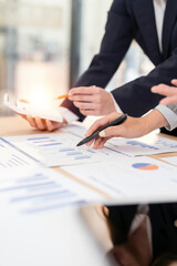 Close-up of co-workers sitting at desk using laptop and tablet, discussing business growth graph