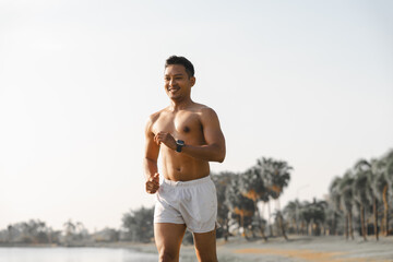 A male athlete enjoys a morning run in the park, smiling and exercising outdoors. Embracing fitness and happiness, he maintains a healthy lifestyle, feeling energized and positive in nature.