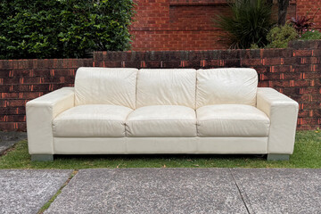 empty three seater leather sofa couch outdoors on nature strip in front of brick wall ready for...