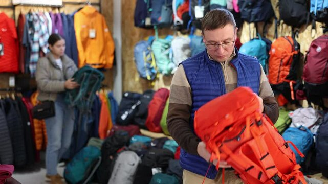 Man view decide on winter backpack for walking tour. Buyer check reliability of locks and zippers, capacity of pockets and number of compartments and compartments. 