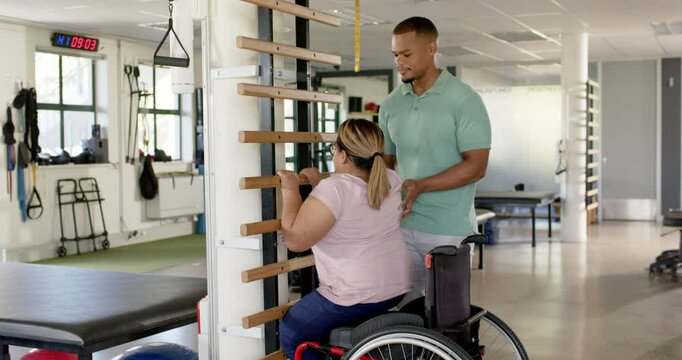 Assisting woman with paraplegia in wheelchair during rehabilitation exercise in therapy center