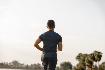 A male athlete enjoys a morning run in the park, smiling and exercising outdoors. Embracing fitness and happiness, he maintains a healthy lifestyle, feeling energized and positive in nature.