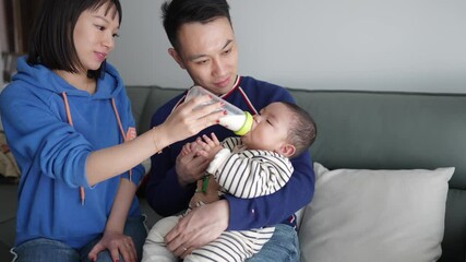 A 6 -month -old baby, Shanghai, China, and grandmother live. They give their baby drinking milk on the sofa of the apartment living room.
