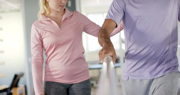 Walking on parallel bars, man in rehabilitation therapy with female therapist