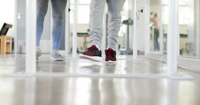 Walking on parallel bars, person in rehabilitation with therapist in gym