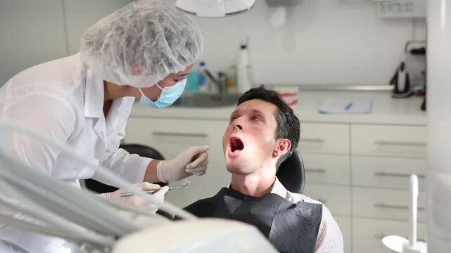 Man is sitting in armchair during dental diagnosis at dentist appointment. Girl doctor conducts examination procedure, identifies problem areas and tests sensitivity of teeth