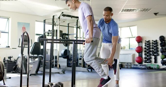 Using parallel bars for rehabilitation exercise, man with disability supported by therapist