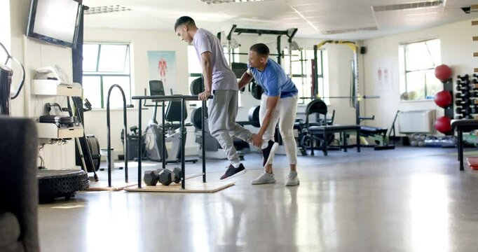 Assisting man with disability, trainer supporting during parallel bars exercise