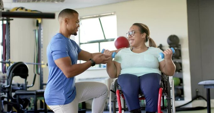 Assisting woman with paraplegia in wheelchair, therapist guiding exercise with dumbbells in rehab