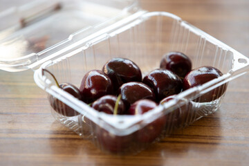 Cherries in a plastic box on a wooden table. 