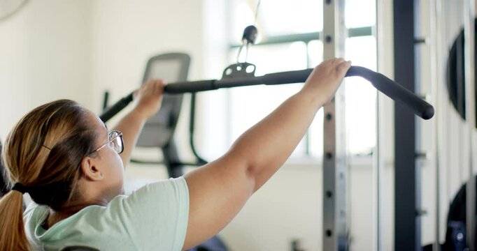 Using lat pulldown machine, woman with disability exercising in gym for rehab