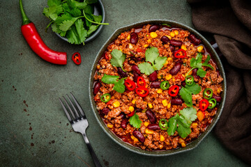 Chili con carne with minced beef, beans, paprika, corn, cilantro, jalapeno pepper in tomato sauce, tex-mex cuisine in green frying pan, top view