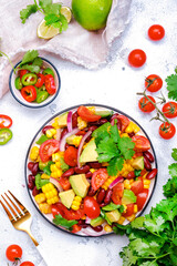 Mexican vegan corn salad with red beans, avocado, tomatoes, onion and cilantro. White background, top view