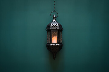 Black hanging lantern with light on green background for the Muslim feast of the holy month of Ramadan Kareem.